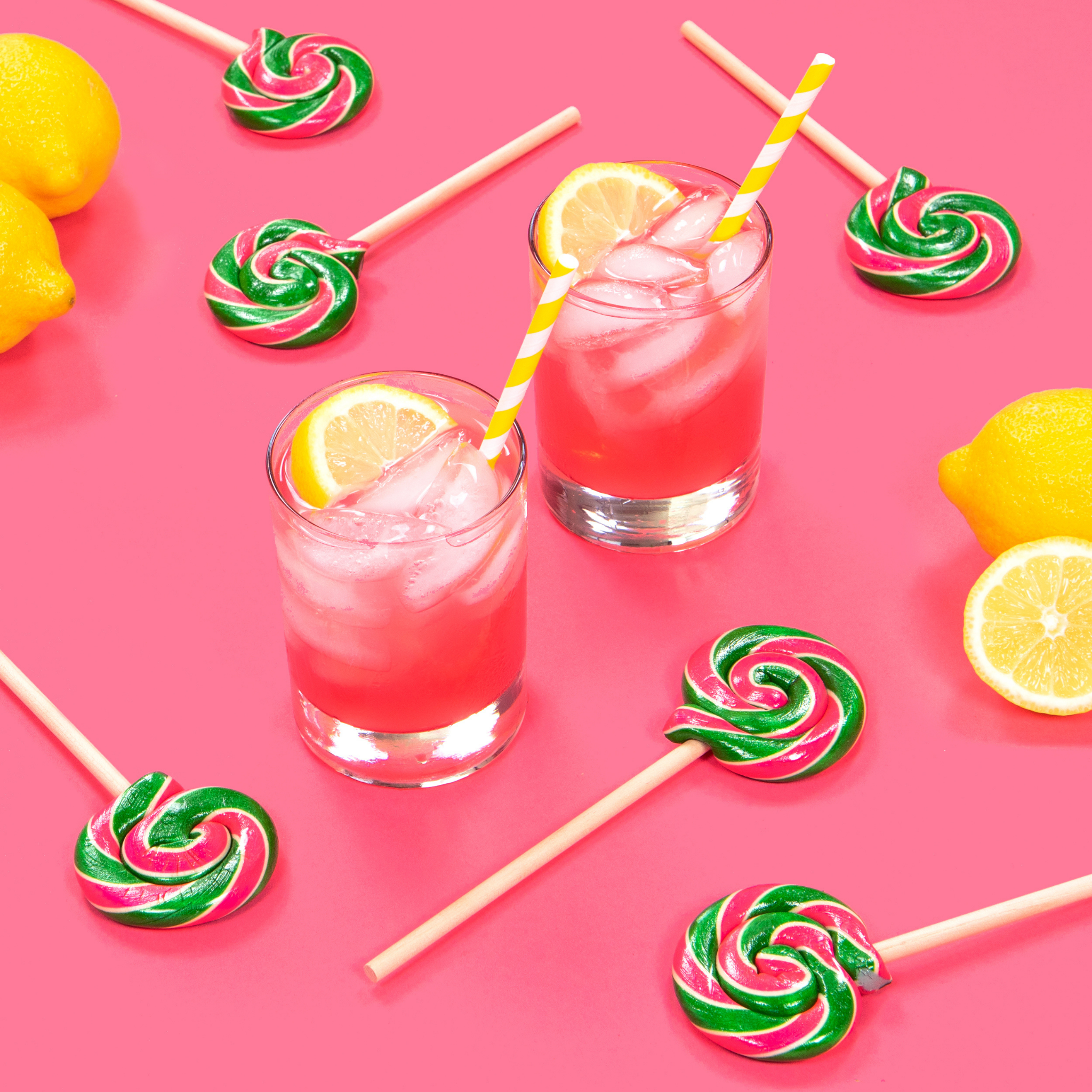 pink lemonade lollipops with two pink lemonade drinks and lemons on a pink background