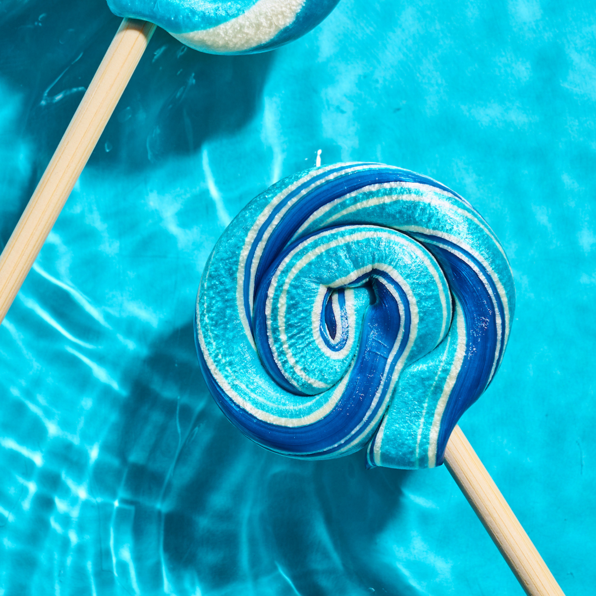 Blue Raspberry Lollipop sitting on a shimmering blue pool