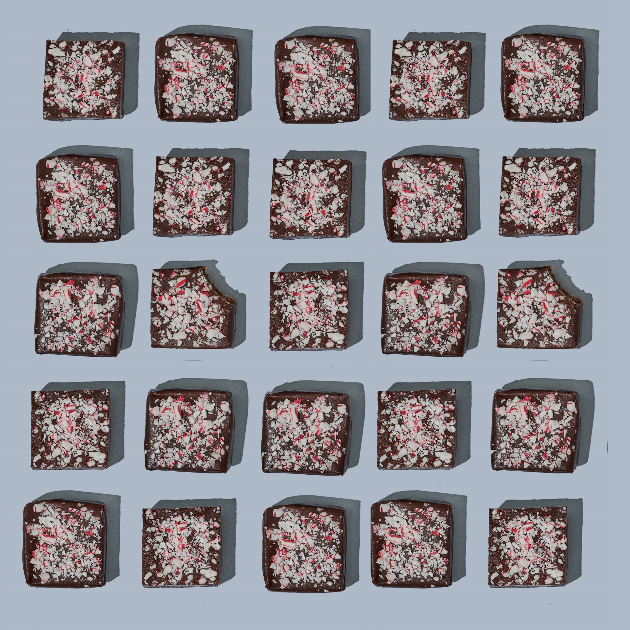 An array of chocolate peppermint caramels with visible peppermint sprinkles on top, arranged in a grid pattern on a light blue background.